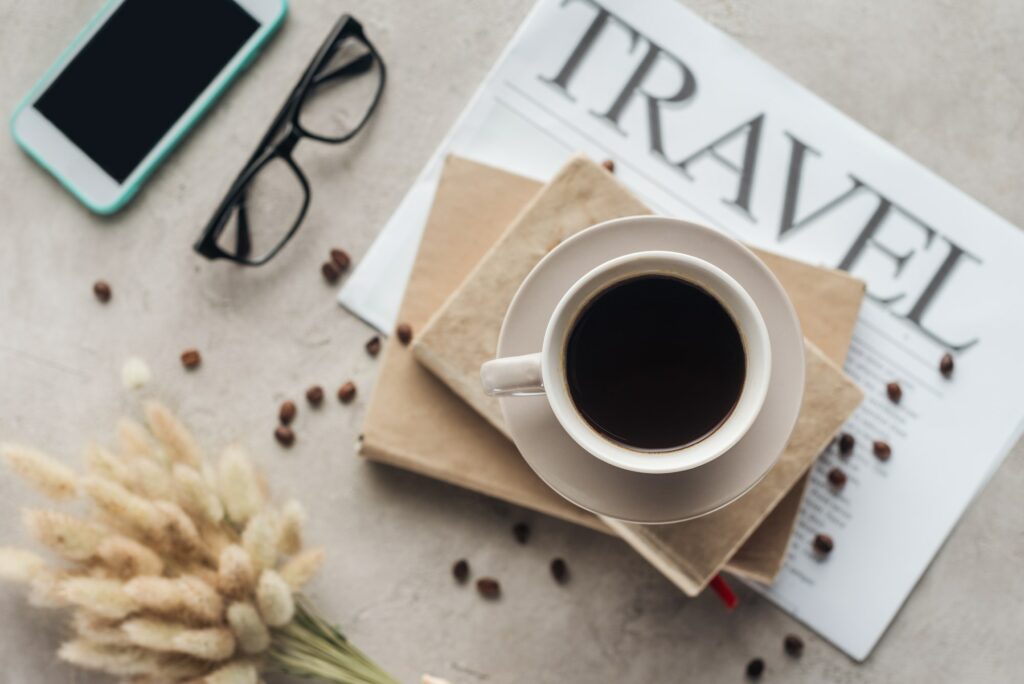 top view of cup of coffee standing on books and newspaper with travel inscription on concrete