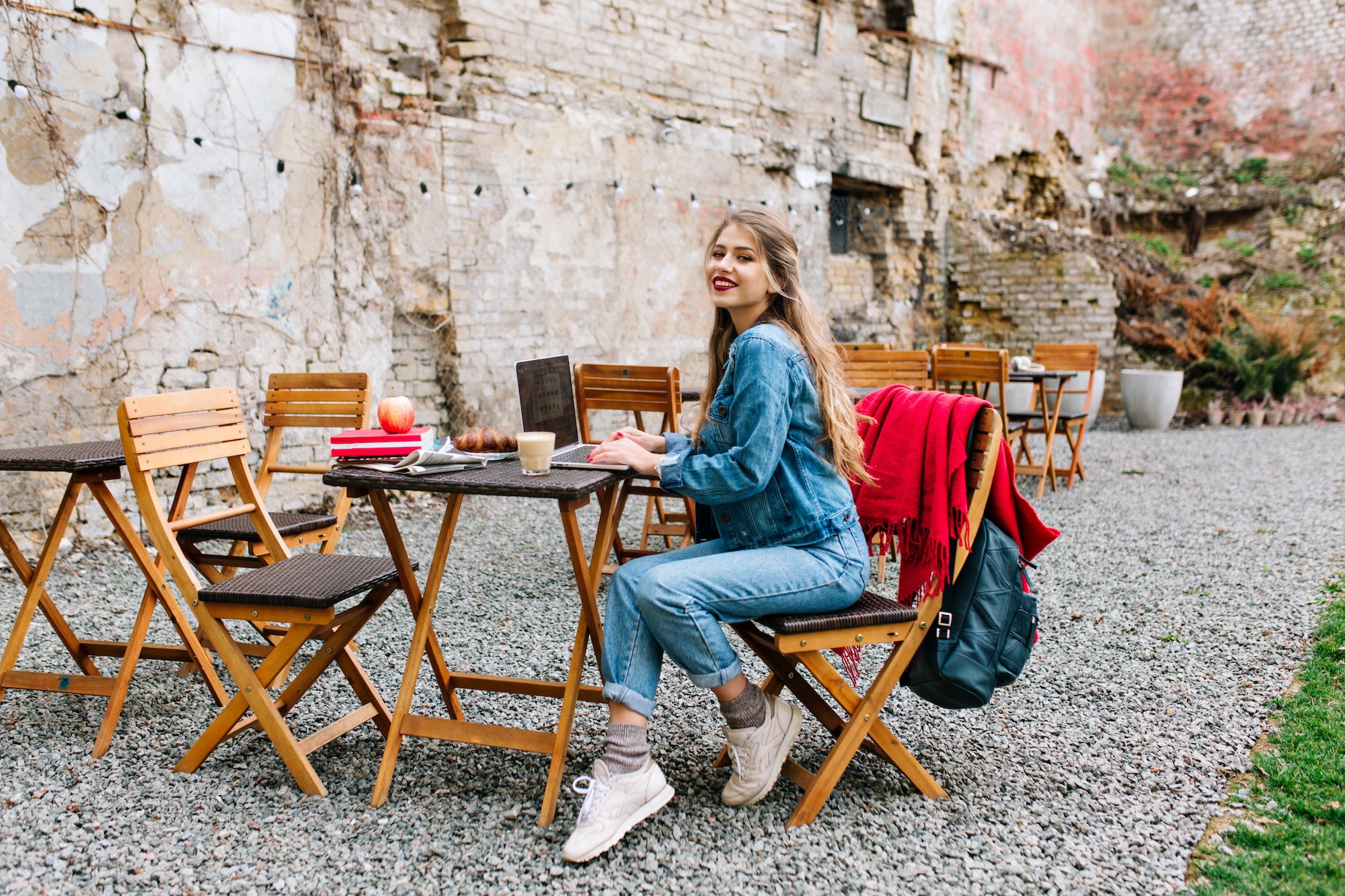 Charming blonde female freelancer using laptop for remote job during breakfast in the outdoor cafe.